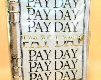 Puede incluir: Un archivador de plástico transparente con una cremallera dorada y un inserto de papel blanco con las palabras "PAY DAY" repetidas en letras doradas.