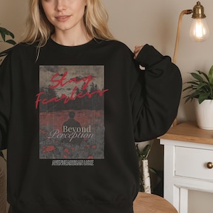 May include: Black crew neck sweatshirt with a graphic design. The design features the words "Stay Fearless" in red script above the words "Beyond Perception" and the text "AVENUE ARTISAN LUXE". The graphic is set against a landscape backdrop.