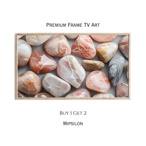 May include: A close-up of a collection of pink and white stones with a grey stone in the background. The stones are arranged in a random pattern on a white surface. The image is framed in a light wood frame. The text "PREMIUM FRAME TV ART" is at the top of the image. The text "BUY 1 GET 2" and "MIPSILON" are at the bottom of the image.