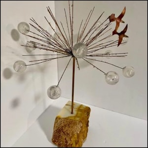 May include: A modern sculpture with a copper wire base and clear glass orbs. The sculpture is mounted on a brown and white marble base. Two copper birds are flying above the orbs.