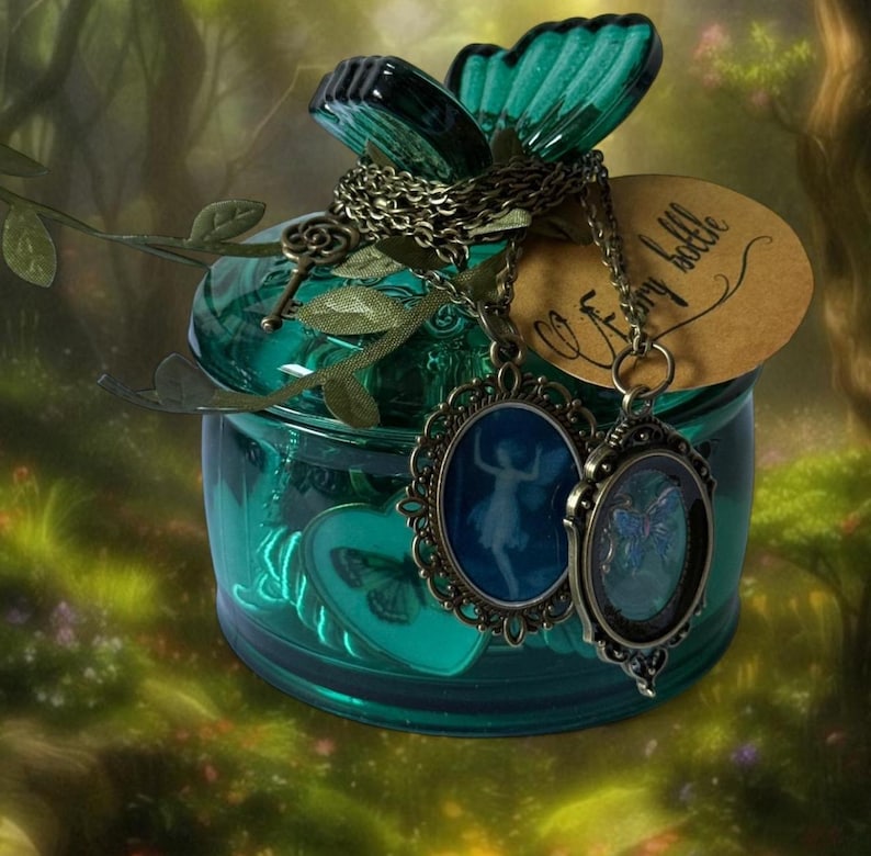 May include: A teal glass jar with a butterfly-shaped lid and two pendant necklaces. The pendants feature fairy silhouettes in oval frames. A tag reads "fairy bottle". The jar is decorated with leaf accents.