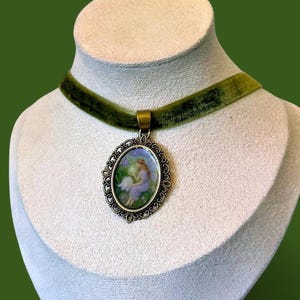 May include: A vintage-style choker necklace featuring a green velvet ribbon and a bronze-toned pendant. The oval pendant showcases a miniature painting of two figures in a garden setting. The necklace is displayed on a mannequin.