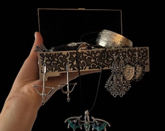 May include: A decorative wooden box with ornate carvings, filled with various silver-toned jewelry. The collection includes necklaces with dragon pendants, bracelets, and earrings. The box is held against a black background.