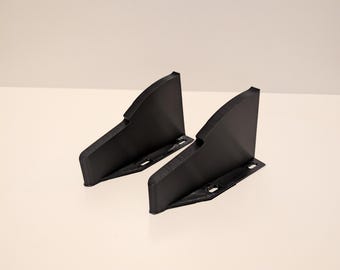 May include: Two black, angular brackets with mounting holes are displayed against a white background. The brackets have a curved top edge and a flat base. They appear to be made of a rigid material, possibly plastic or metal, and are designed for structural support.