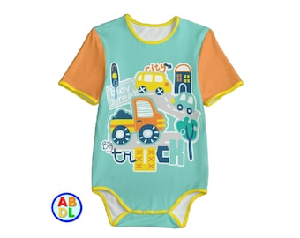 Puede incluir: Un body de bebé turquesa con mangas cortas y ribete amarillo. El body presenta un gráfico colorido de una escena de ciudad con un camión grande, un autobús escolar, un automóvil y un semáforo. El texto "Big Truck" y "Busy Street" está impreso en el body.