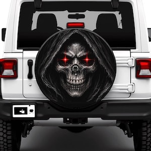 May include: A white SUV featuring a circular spare tyre cover on the rear. The cover displays a detailed black and white graphic of a hooded skull with glowing red eyes. The vehicle has red taillights and a rectangular license plate area.