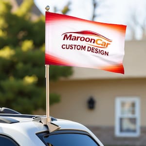 Op de afbeelding: Een witte autovlag met de tekst "Maroon Car CUSTOM DESIGN" in bordeauxrood en oranje. De vlag heeft een rood-oranje verloopontwerp en is gemonteerd op een zilveren paal die aan een auto is bevestigd.