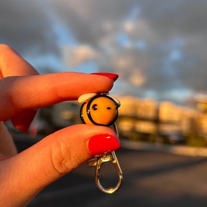 May include: A small yellow and black bee keychain with a white wing. The bee has a black smiley face.