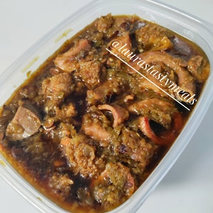 May include: A clear plastic container filled with a dark brown stew with green peppers and meat. The stew is topped with a layer of green peppers. The container has a white background and the text "@laurastastymeals" is written on the side.