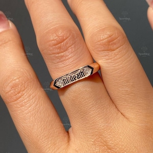 May include: A gold ring with the words "Til Death" set with diamonds. The ring is worn on a person's finger.
