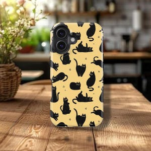 May include: A phone case with a yellow background featuring a repeating pattern of black cat silhouettes in various poses and small star shapes. The case has a camera cutout and is sitting on a wooden surface.
