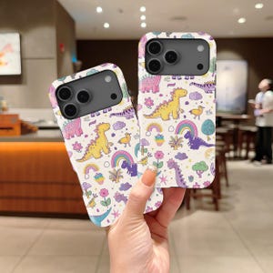 May include: Two mobile phone cases featuring a repeating pattern of colourful dinosaurs, rainbows, flowers, and clouds on a white background. The cases have a black camera cutout area and are designed to fit a smartphone with a multi-lens camera system.