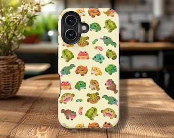 May include: A phone case featuring a repeating pattern of colorful cartoon frogs in various poses. The frogs are in shades of green, orange, pink, and brown, set against a light yellow background. The case has a camera cutout.