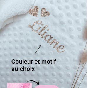 Peut inclure: Une couverture blanche à texture alvéolée avec le prénom Liliane écrit en lettres cursives à paillettes or rose, accompagné de deux petits cœurs à paillettes. L'image contient le texte Couleur et motif au choix et Existe aussi en rose.