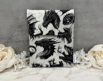 Op de afbeelding: Een wit en zwart tissueboxhoesje met drakenmotief. De hoes heeft een herhalend patroon van gedetailleerde drakenillustraties. De draken worden in verschillende poses afgebeeld, met vleugels, hoofden en klauwen. De tissueboxhoes is gemaakt van stof.