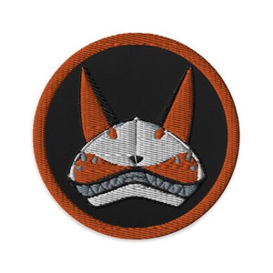 May include: Embroidered patch featuring a stylized fox head design. The patch has a black background with an orange border. The fox head is white, orange, and gray, with pointed ears and a detailed snout.