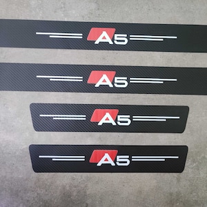May include: Four black carbon fibre car door sill protectors with a red and white "A5" logo.
