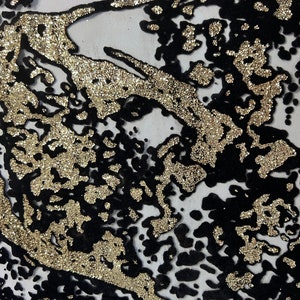 Könnte beinhalten: Schwarzer und goldener Stoff mit einem glitzernden, abstrakten Muster. Der Stoff hat eine mesh-artige Textur und ist mit goldenem Glitzer verziert.