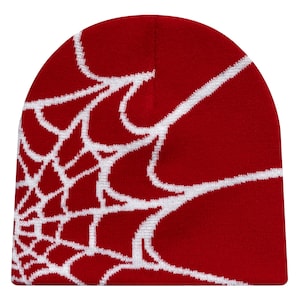 Puede incluir: Un gorro rojo con un diseño de telaraña blanca. El gorro está hecho de un material de punto suave. El diseño de telaraña cubre el lado izquierdo del gorro.