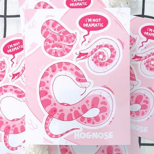 May include: Pink and white illustration of a hognose snake on a pink background. The snake is in various poses, with the text "I'M NOT DRAMATIC" in a speech bubble. The word "HOGNOSE" is also visible.