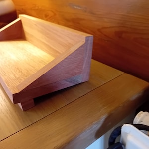 Peut inclure: Un organiseur de bureau en bois fait à la main avec une finition naturelle. L'organisateur comprend un plateau rectangulaire avec un dos incliné et une petite base. Le grain du bois est visible, mettant en valeur la beauté naturelle du matériau.