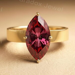 Op de afbeelding: Een gouden ring met een grote, marquise-geslepen, dieprode edelsteen. De ring heeft een brede, effen gouden band. De edelsteen is gezet met vier kleine gouden pootjes. De ring wordt getoond op een neutrale, getextureerde ondergrond.