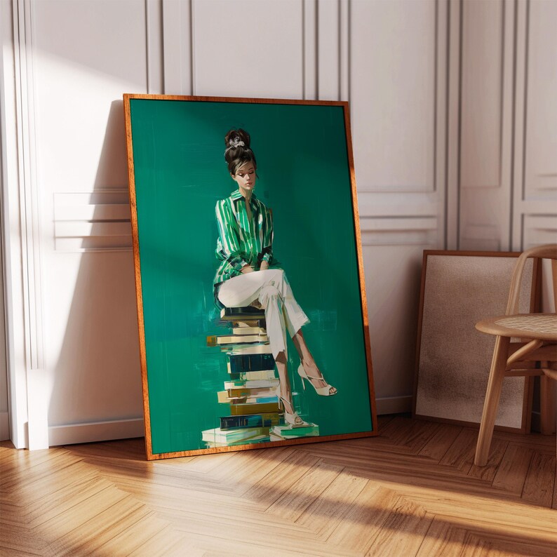 May include: A framed art print featuring a woman in a green and white striped jacket and white pants, seated atop a stack of books. The artwork has a green background and a gold frame. The print is leaning against a white wall on a wooden floor.
