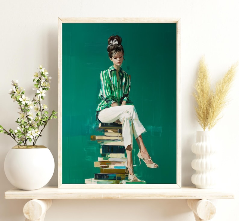 May include: A framed art print depicts a woman in a green and white striped shirt and white pants, seated on a stack of books. The artwork has a green background and the woman is wearing high heels. The print is displayed on a white shelf.