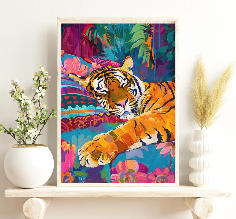 K&ouml;nnte beinhalten: Gerahmter Kunstdruck eines schlafenden Tigers. Der Tiger mit orangefarbenen und schwarzen Streifen liegt auf einer bunten, gemusterten Oberfl&auml;che. Der Hintergrund zeigt &uuml;ppiges gr&uuml;nes Laub.