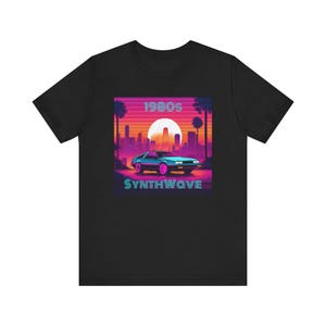 Könnte beinhalten: Schwarzes T-Shirt mit einem Retro-Design aus den 80ern, das ein blaues Auto zeigt, das durch eine Sonnenuntergangs-Stadtlandschaft fährt. Der Text "1980s SYNTHWAVE" ist unter dem Auto gedruckt.