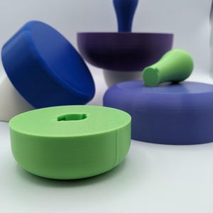 Puede incluir: Un conjunto de juguetes apilables de colores hechos de pl&aacute;stico. Los juguetes tienen forma de hongo con tapas de diferentes colores y tallos blancos. El conjunto incluye un hongo azul, verde y morado.