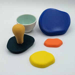 Peut inclure: Ensemble d'objets de formes abstraites et color&eacute;es. Comprend une base vert fonc&eacute; avec une poign&eacute;e marron clair, un bol blanc et turquoise, une grande forme bleue et des formes orange et jaune plus petites. Sur fond blanc.