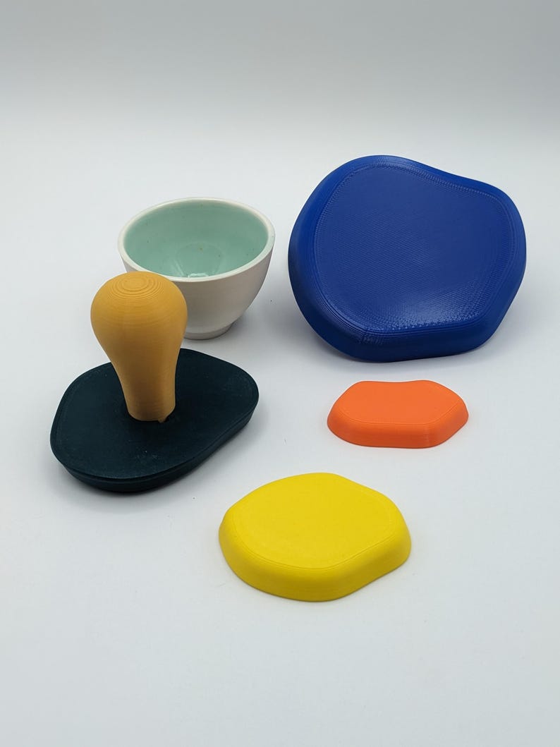 Peut inclure: Ensemble d'objets de formes abstraites et color&eacute;es. Comprend une base vert fonc&eacute; avec une poign&eacute;e marron clair, un bol blanc et turquoise, une grande forme bleue et des formes orange et jaune plus petites. Sur fond blanc.