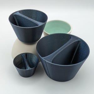Può includere: Tre ciotole in ceramica blu con una sezione divisa. Le ciotole sono di dimensioni diverse e sono impilate l'una sull'altra.