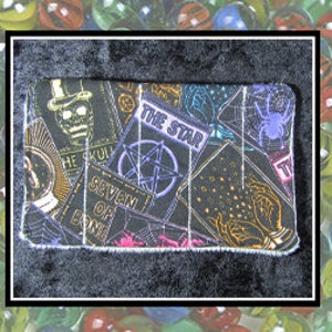 Könnte beinhalten: Eine schwarze Stofftasche mit Reißverschluss, die mit einer bunten Collage von Tarotkarten mit verschiedenen Symbolen und Bildern verziert ist, darunter ein Schädel, ein Pentagramm und ein Stern.