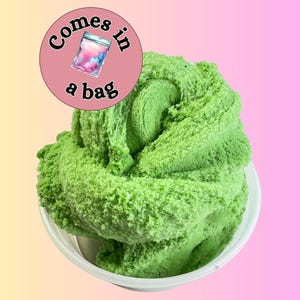 May include: A large, textured, lime green slime in a white bowl. A pink circle with the text "Comes in a bag" and a graphic of a baggie is in the upper left corner. The background is a gradient of yellow and pink.