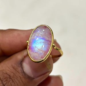 Op de afbeelding: Een gouden ring met een ovale, iriserende maansteen. De maansteen toont een mix van roze, blauwe en witte tinten. De ring heeft een gepolijste gouden zetting, wat zorgt voor een klassieke en elegante uitstraling.