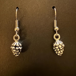 May include: A pair of silver dangle earrings featuring a small pine cone design.