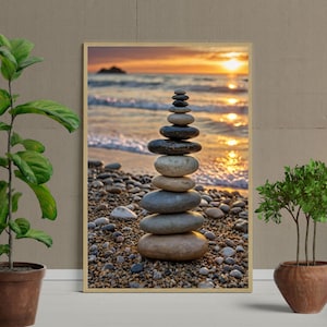 Op de afbeelding: Een ingelijste prent van een strandscène bij zonsondergang. Een stapel gladde, afgeronde stenen staat op de voorgrond. De stenen zijn in verschillende tinten grijs en bruin. De achtergrond toont de oceaan en een gouden zonsondergang.