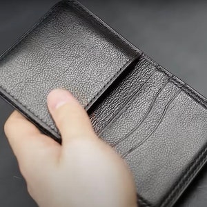 Può includere: Un portafoglio in pelle nera con più slot per carte e una patta.