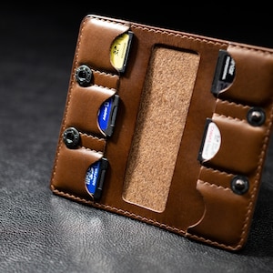 May include: A brown leather case with multiple slots for holding game cartridges. The case has a flap that closes with a snap.