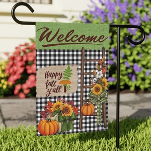 May include: A welcome garden flag with a black and white checkered pattern. The flag features a wooden ladder with a bow, sunflowers, cotton bolls, and pumpkins. The text "Welcome" is written in brown cursive lettering at the top of the flag. The text "Happy fall y'all" is written on a brown sign with a mushroom and a fern.