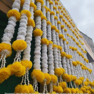 May include: A wall decorated with white and yellow paper flower garlands. The garlands are strung together in a repeating pattern.