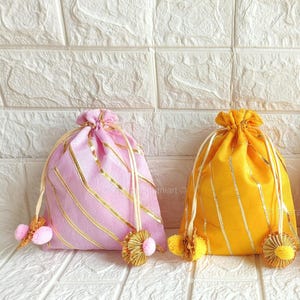 Può includere: Tre sacchetti con coulisse con strisce dorate e pon pon. I sacchetti sono rosa, giallo e fucsia.