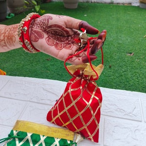 Puede incluir: Dos pequeñas bolsas decorativas con ribetes dorados. Una bolsa es roja con patrones de diamantes dorados y la otra es verde con rayas diagonales doradas.