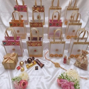 May include: A collection of twelve small, translucent white gift bags with gold trim and colorful embroidered accents, accompanied by a gold gift box, assorted chocolates, a decorative beaded bracelet, two small glass vials, and floral bouquets.