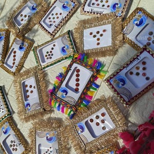 May include: An overhead shot displays multiple decorative bindi sets. Each set is presented in a rectangular or square package, adorned with gold trim and colorful accents. The packages contain various sizes and colors of bindis, with some featuring peacock designs.