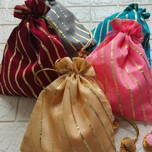 Puede incluir: Cinco pequeñas bolsas de cordón con rayas doradas en una variedad de telas de colores. Las bolsas están dispuestas en semicírculo sobre una superficie de azulejos blancos.