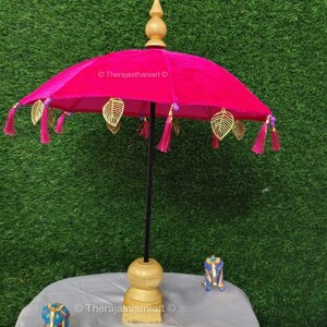 K&ouml;nnte beinhalten: Ein rosa Samt-Schirm mit goldenen Blatt-Akzenten und rosa Quasten. Der Schirm steht auf einem Holzst&auml;nder mit goldener Basis.