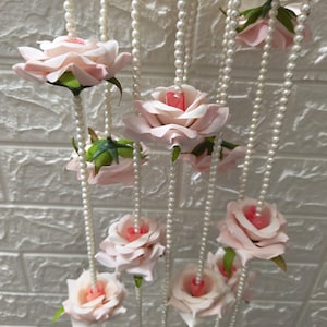May include: A pink flower garland with pearl beads hanging from the ceiling. The garland is made of artificial flowers and pearls.